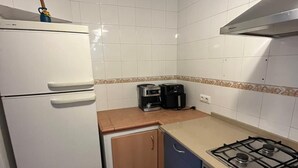 Uma cozinha compacta com paredes de azulejos brancos, piso estampado, geladeira branca, fogão e torradeira.