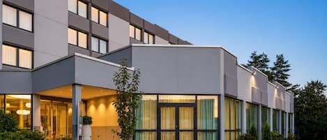 A modern hotel with a flat facade, large windows, and a well-maintained garden.