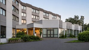 Un hotel moderno con fachada curva, amplias ventanas y entrada ajardinada.