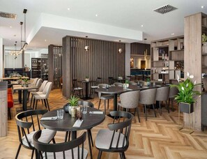 Um restaurante moderno com mesas redondas, cadeiras e um padrão de piso em espinha de peixe.