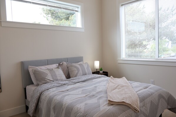 A bedroom with a bed, a nightstand, a lamp, and a window with blinds.