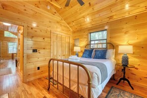 A wooden cabin bedroom with a bed, bedside table, lamp, and a window. - Fern and Timber (Murphy)