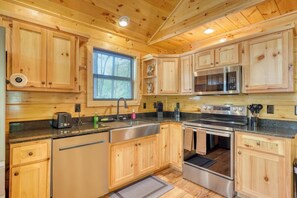 A wooden cabin-style kitchen with a sink, stove, microwave, and cabinets. - Fern and Timber (Murphy)