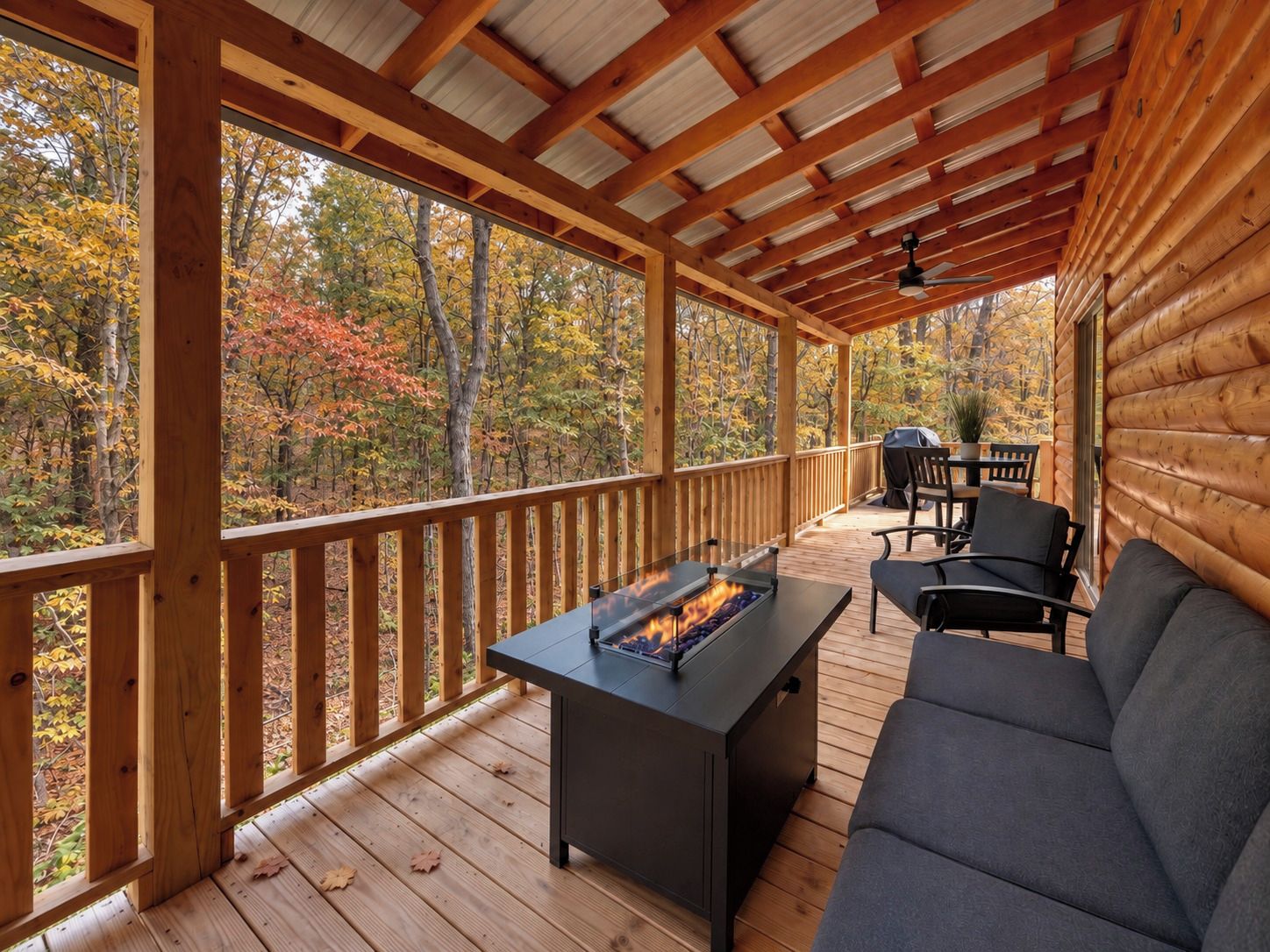 Une terrasse extérieure couverte, dotée d’un foyer, de sièges et offrant une vue sur le feuillage automnal.