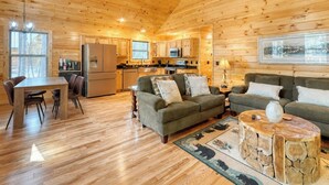 A cozy cabin interior with wooden walls, a dining area, a kitchen, and a living room furnished with sofas and a coffee table. - Fern and Timber (Murphy)
