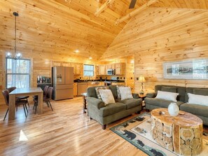 A cozy cabin interior with wooden walls, a dining area, a kitchen, and a living room furnished with sofas and a coffee table. - Fern and Timber (Murphy)