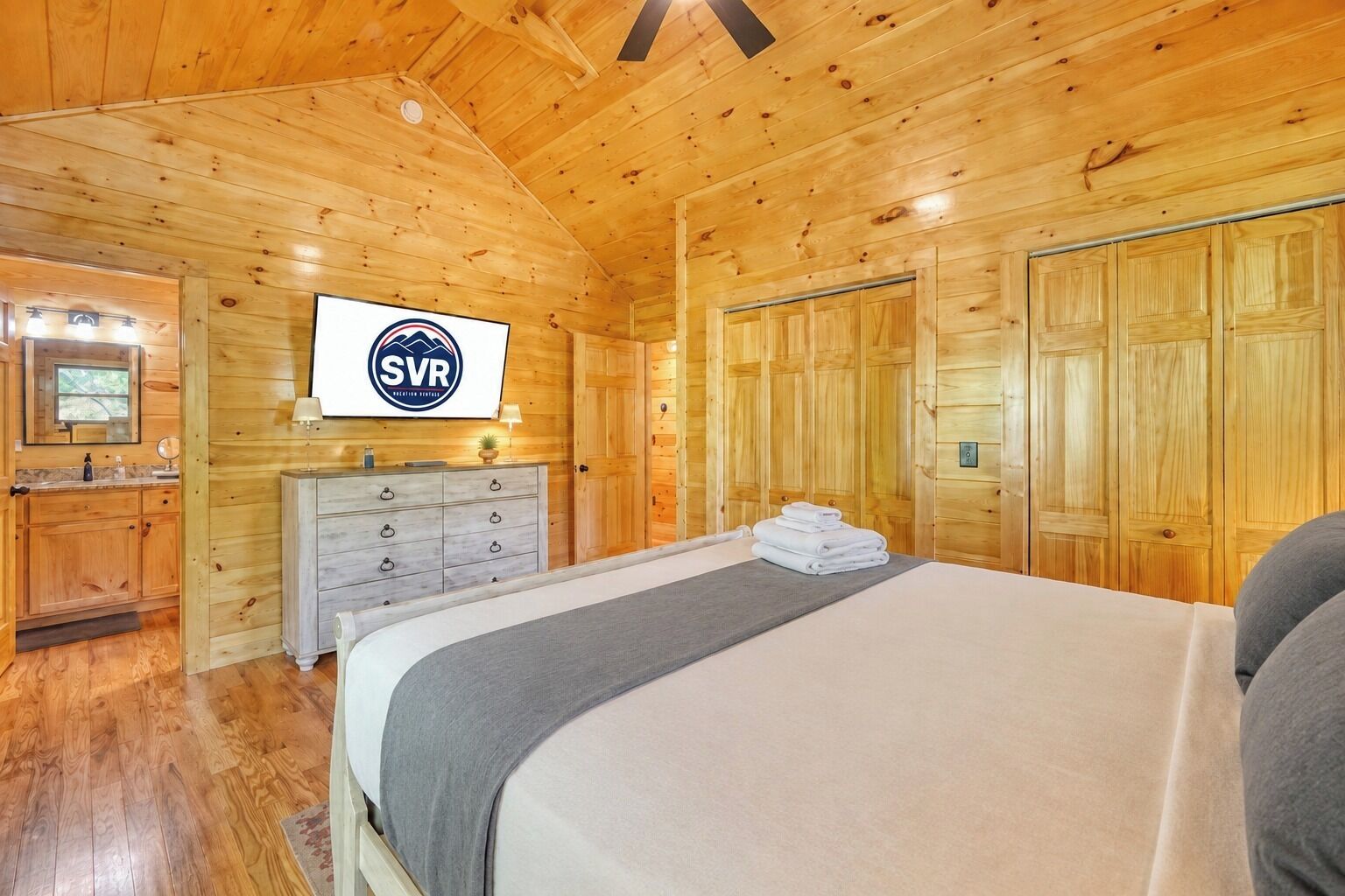 Una habitación de cabaña de madera con cama, cómoda, espejo y televisor.