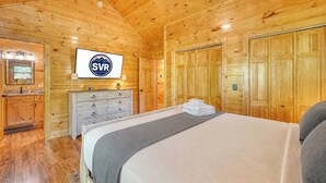 A wooden cabin room with a bed, a dresser, a mirror, and a television. - Fern and Timber (Murphy)