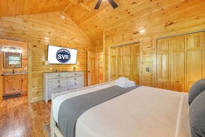 A wooden cabin room with a bed, a dresser, a mirror, and a television. - Fern and Timber (Murphy)