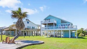 Ein strandnahes Anwesen mit einem zweigeschossigen Gebäude, einer Holzterrasse und einer Palme.