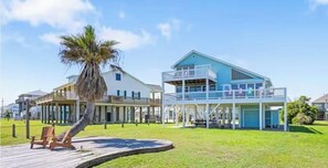 A beachfront property with a two-story building, a wooden deck, and a palm tree. - Papa Ric's Happy Place (Bolivar Peninsula)