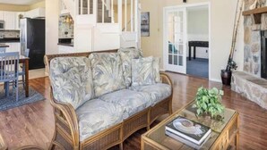 Ein Wohnzimmer mit einem Rattan-Sofa, einem Glastisch mit einem Buch und einem Kamin.