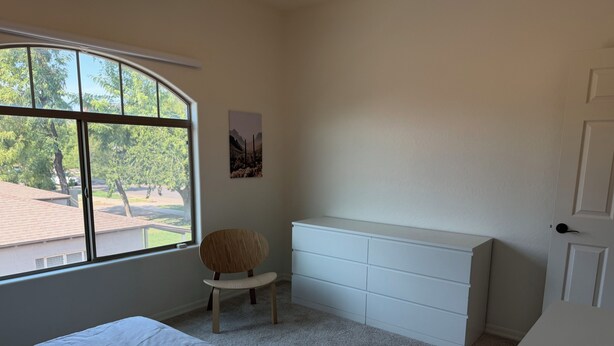 A bedroom with a bed, a chair, a dresser, and a window with a view of trees and a building. - ASU Parent, Alumni, Sports Fan, Traveler - this is your place. (Tempe)