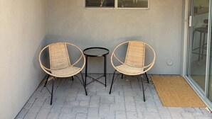 A small outdoor seating area with two wicker chairs and a table, a window, and a door to a covered patio. - ASU Parent, Alumni, Sports Fan, Traveler - this is your place. (Tempe)