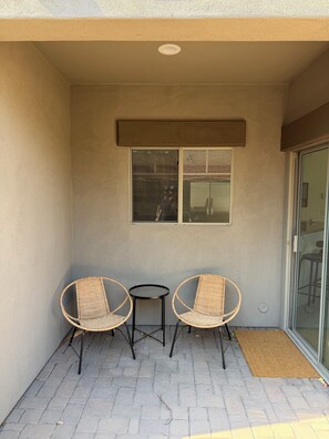 A small outdoor seating area with two wicker chairs and a table, a window, and a door to a covered patio. - ASU Parent, Alumni, Sports Fan, Traveler - this is your place. (Tempe)