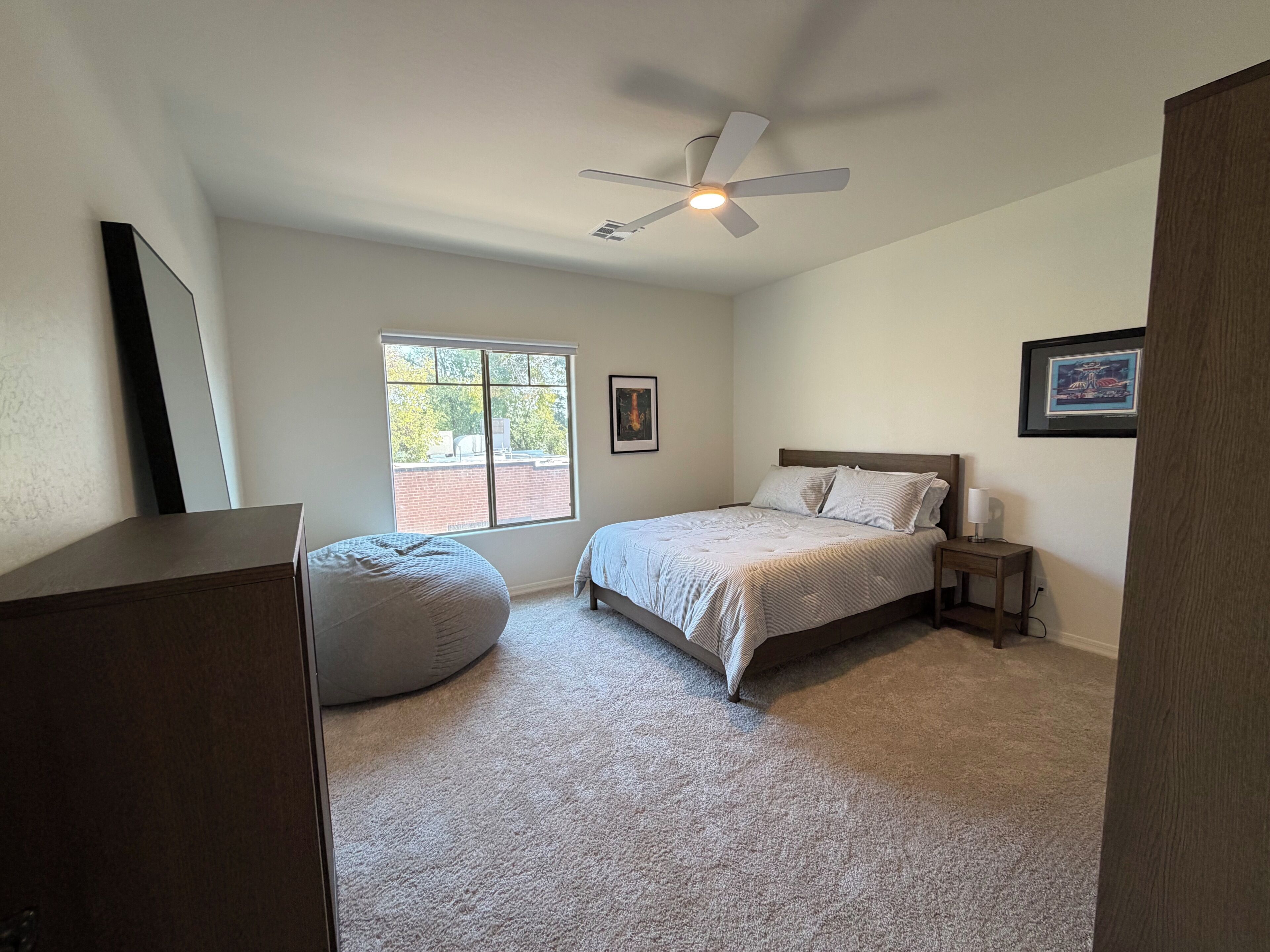A bedroom with a bed, a standing lamp, a ceiling fan, a window, and a wall-mounted picture.