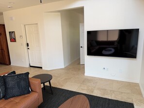 A living room with a large flat-screen TV mounted on the wall, a brown leather sofa, a small round table, and a black woven rug. - ASU Parent, Alumni, Sports Fan, Traveler - this is your place. (Tempe)