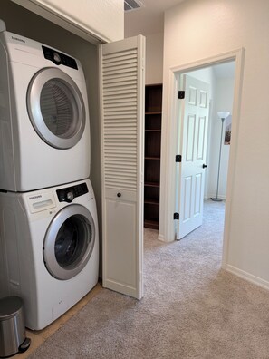 A laundry area with two white Samsung washing machines, a closed white closet, and a carpeted hallway leading to a door. - ASU Parent, Alumni, Sports Fan, Traveler - this is your place. (Tempe)