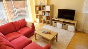 Ein Wohnzimmer mit einem roten Sofa, einem Holztisch, einem Bücherregal und einem Fernseher auf einem Schrank.