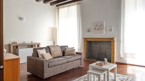 A living room with a sofa, a small table, a fireplace, and a window with curtains. - [Historic Center] Elegant one-bedroom apartment with a balcony (Brescia)