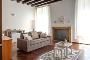 A living room with a sofa, a small table, a fireplace, and a window with curtains. - [Historic Center] Elegant one-bedroom apartment with a balcony (Brescia)