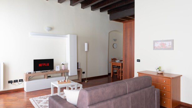 A modern living room with a flat-screen TV, a sofa, a wooden cabinet, and a dining area with a table and chairs. - [Historic Center] Elegant one-bedroom apartment with a balcony (Brescia)