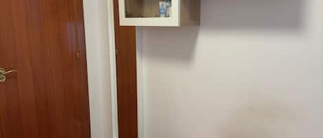 A room with a bed, a wooden wardrobe, and a white cabinet with a shelf.