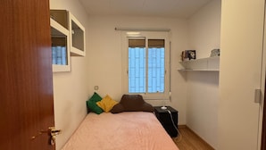 A bedroom with a bed, a window, a bedside table, and a shelf with books. - Barcelona Room – Temporary Sublet €40/day: 10% discount for longer stays (Spain)