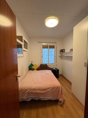 A bedroom with a bed, a window, a bedside table, and a shelf with books. - Barcelona Room – Temporary Sublet €40/day: 10% discount for longer stays (Spain)