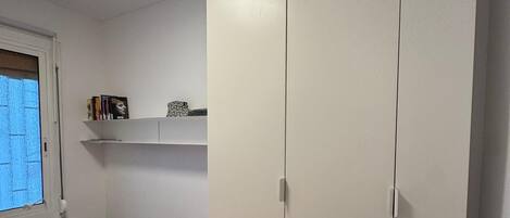 Een slaapkamer met een bed, een kledingkast, een plank met boeken en een bureau met een lamp.