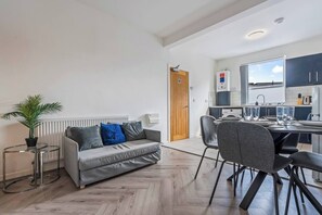 A modern living room with a grey sofa, a small side table, and a potted plant. - 2 Bed Duplex | Jewellery Quarter | Sleeps 4 (West Midlands)