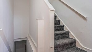 Eine schmale Treppe mit Handlauf und Teppichstufen, die zu einer Zwischenebene führt.