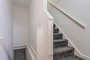 Eine schmale Treppe mit Handlauf und Teppichstufen, die zu einer Zwischenebene führt.