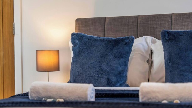 Ein Hotelzimmer mit einem Bett, zwei Kissen, einer Nachttischlampe und einem Handtuch.
