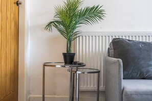Ein Zimmer mit einem grauen Sofa, einem kleinen runden Tisch mit einem Topf und einer Heizung.