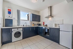 A modern kitchen with a built-in washing machine, microwave, oven, and a stainless steel range hood. - 2 Bed Duplex | Jewellery Quarter | Sleeps 4 (West Midlands)