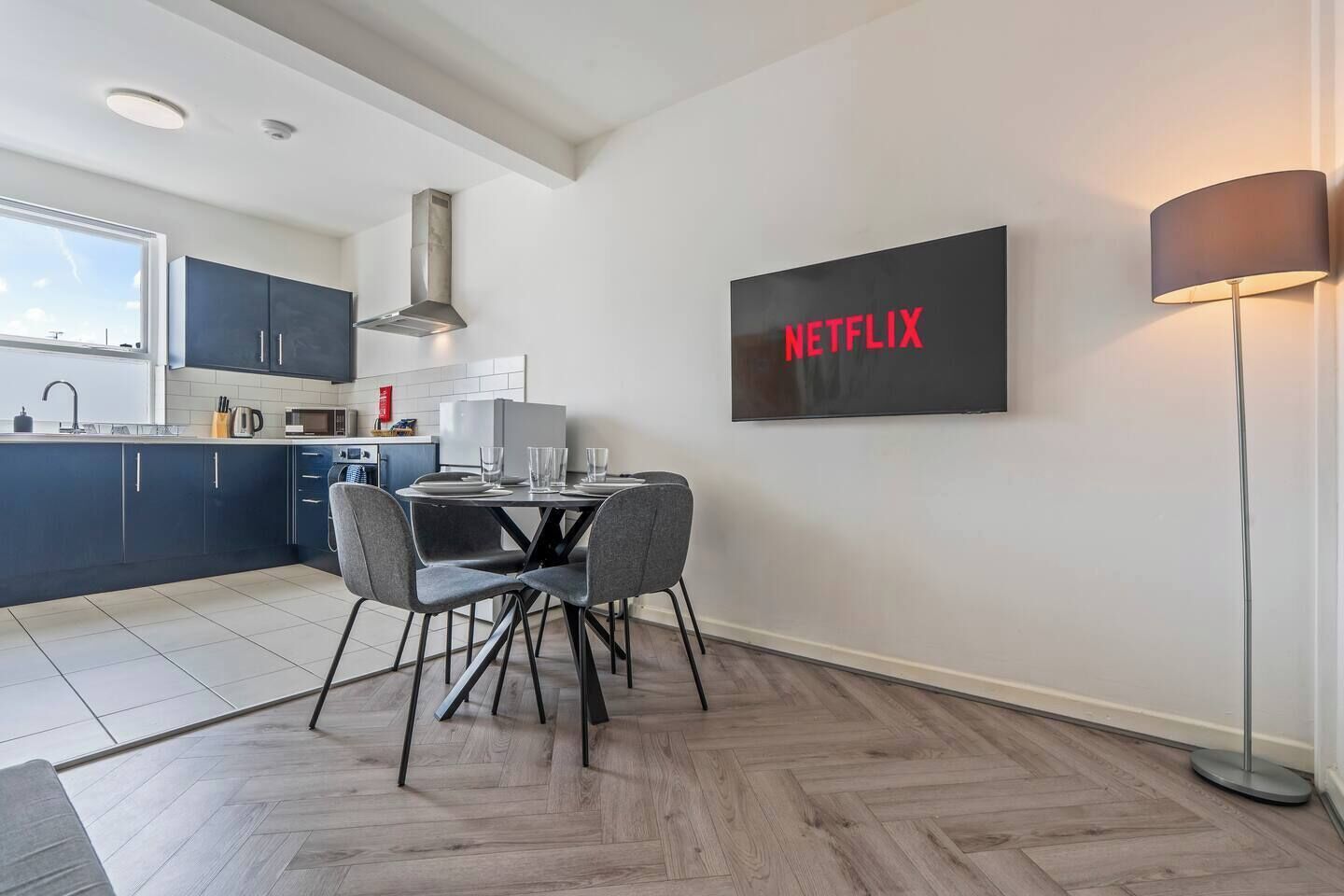 Una cocina moderna con armarios oscuros, una mesa de comedor con sillas, un microondas y un cartel negro grande con la palabra 'NETFLIX' en letras rojas.