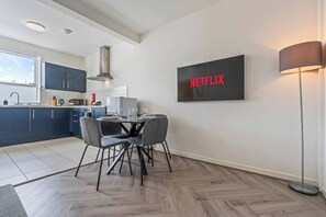 A modern kitchen with dark cabinets, a dining table with chairs, a microwave, and a large black sign with 'NETFLIX' in red letters. - 2 Bed Duplex | Jewellery Quarter | Sleeps 4 (West Midlands)