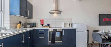 A modern kitchen with dark cabinetry, a stainless steel range hood, a microwave, a toaster, and a refrigerator.