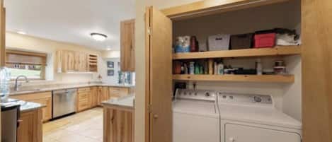 Eine kompakte Küche mit Holzschränken, einer integrierten Waschmaschine und einem Trockner sowie einem Fenster für natürliches Licht.