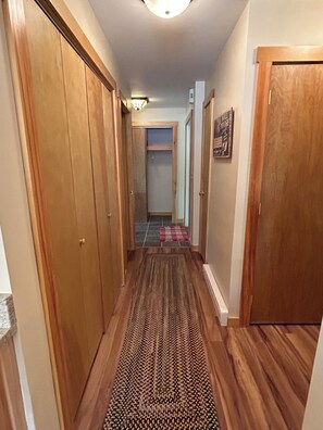 A hallway with wooden floors, a patterned rug, and a door on the right.