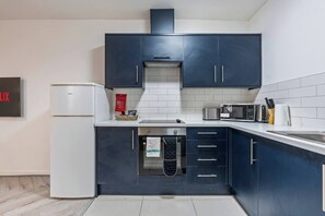 A modern kitchen with dark blue cabinets, a white refrigerator, a microwave, and a toaster. - 1 Bed Flat | Jewellery Quarter | Sleeps 2 (West Midlands)