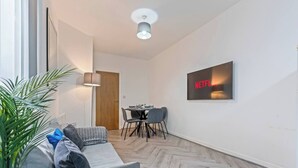Un salon moderne avec un canapé, une table à manger et des chaises, une lampe et un téléviseur fixé au mur qui affiche le logo de Netflix.