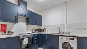 Une cuisine moderne avec des meubles de rangement bleu foncé, un four à micro-ondes, un évier et un lave-linge.