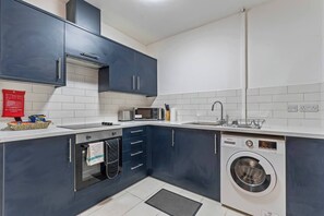 A modern kitchen with dark blue cabinets, a microwave, a sink, and a washing machine. - 1 Bed Flat | Jewellery Quarter | Sleeps 2 (West Midlands)
