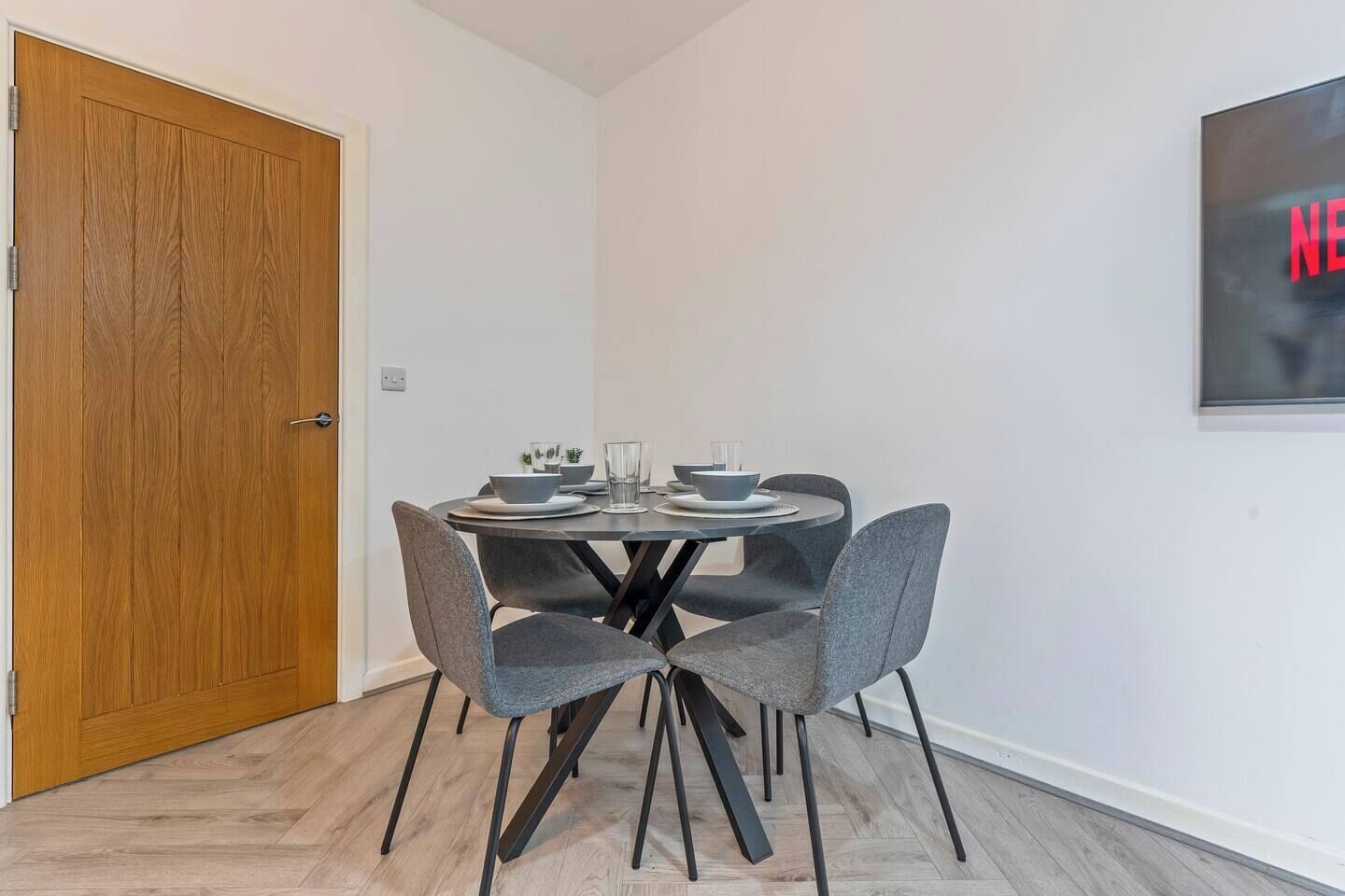 A dining area with a round table, four grey chairs, and a wooden door.
