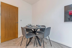 A dining area with a round table, four grey chairs, and a wooden door. - 1 Bed Flat | Jewellery Quarter | Sleeps 2 (West Midlands)