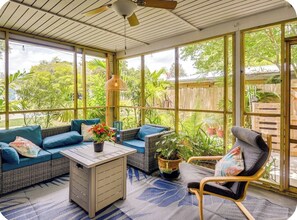 A sunroom with a sofa, chair, and table, surrounded by large windows and plants. - 'Palm Bungalow' Near Downtown St Augustine & Beaches! (St. Augustine)