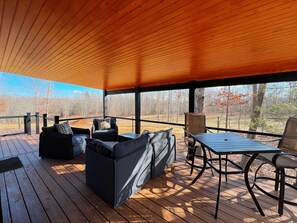 An outdoor deck with wooden flooring, black outdoor furniture, and a view of a forested area. - Bison Farm - Cabin "Brisa" (Culpeper)