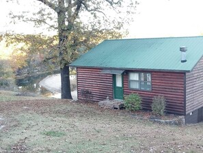 Eine Blockhütte mit einem grünen Dach, einer kleinen Veranda und einem Teich im Hintergrund.